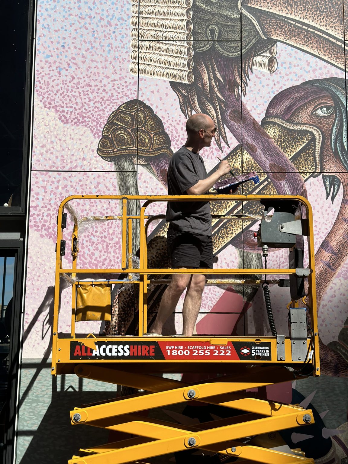 Artist painting a mural using a scissor lift available for all applications from All Access Hire